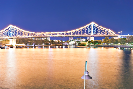 Yellow river and a city bridge illuminated by lights at night with blue sky in the Brisbane City, Queensland, Australia.のeditorial素材
