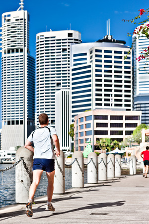 Back view of a young athlete runs on the waterside street to a city with huge white buildingsのeditorial素材
