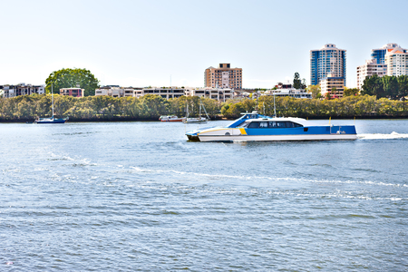 Boat runs on the blue water river  beside tress and the Brisbane City, Queensland, Australia.のeditorial素材