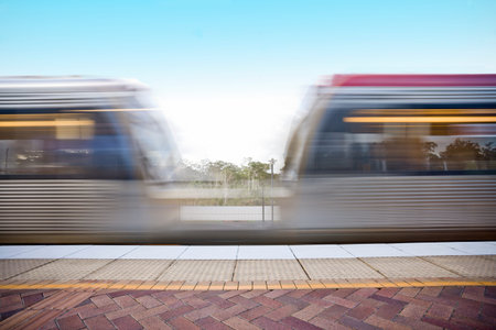 Fast trains moving forward infront of station, sunlight around the area, morning time and rush hours, floor is tiled, sky is clear.の写真素材