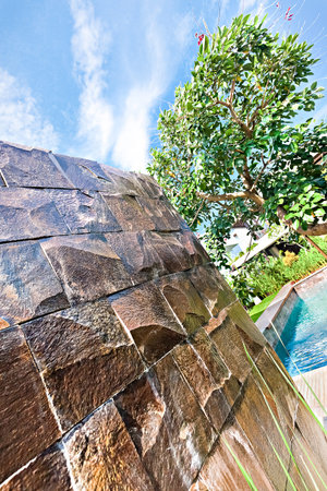 Wet stone wall waterfall turned off in a garden with a tree and blue sky for the background