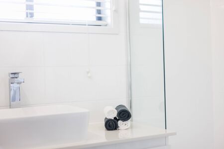 View of a wash basin and a faucet featuring four rolled up towels in black and white kept on the side counterの写真素材