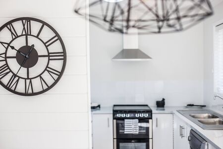 Contemporary design wall clock mounted on the kitchen wall with chimney, sink and oven in the backgroundの写真素材