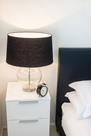 A view of a side table with drawers featuring a lamp shade and an alarm clock kept on top of it