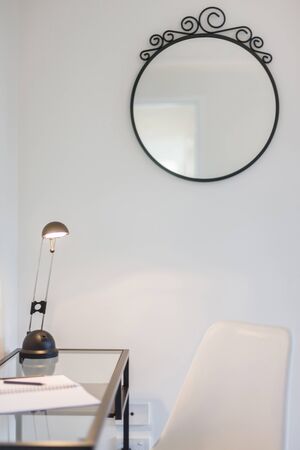 View of a reading area featuring a decorative wall mirror, a glass table, reading lamp and a chairの写真素材