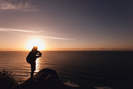 Young woman exercises yoga on a boulder at Burleigh Heads, Queensland, Australia. A female meditating during sunrise over the amazing seascape sceneの写真素材