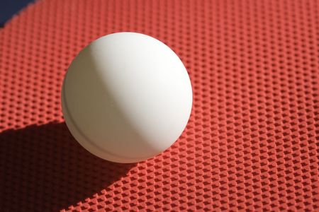 Closeup of a ping pong racket and ball against a dark blue table.の写真素材