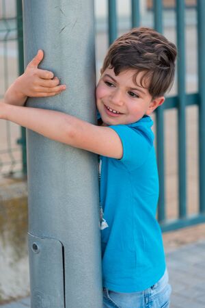 5 year old boy hugging lamppost and smiling with blue t-shirt and jeansの写真素材