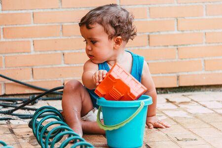 little boy playing with bucket and water at home confinement covid19の写真素材