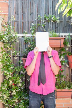 Middle-aged man teleworking in his backyard fuchsia shirt with tie and dark jeansの写真素材