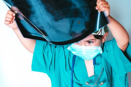 cute kid playing doctor dressed as a surgeon examining an x-rayの写真素材