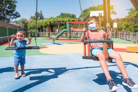 social distancing between two children in the park, the older one wearing a coronavirus maskの写真素材