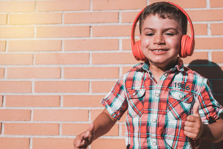 portrait kid listening to music with headphones on brick wall