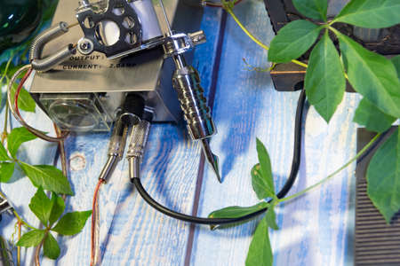 complete equipment of tattooing machines. blue wood and brick background with plant leaves. Selective focus.の写真素材