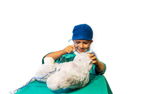 happy child disguised as a surgeon playing doctor operating on a teddy bearの写真素材