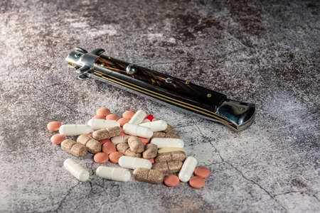 mixed pill and tablet pile next to automatic knife, hazard conceptの写真素材