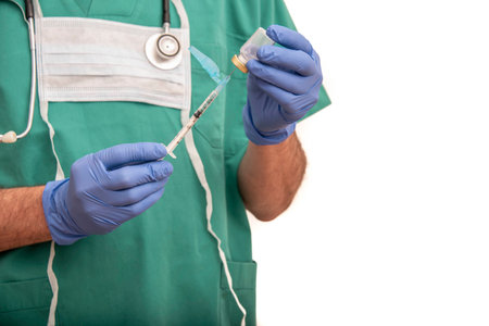 Male nurse carrying vaccine or medication in syringe with safety needle, dressed in green scrubs on...