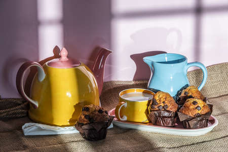 Breakfast with milk and muffins served in a traditional teapot with a yellow and pink color palette.の写真素材