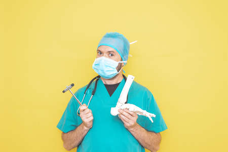 Trauma surgeon wearing an operating theater uniform and stethoscope, checking a skeleton model of a foot, right lower limb, all on a yellow background.の写真素材