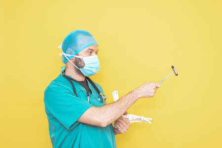 doctor dressed as a surgeon in green with stethoscope and mask on a yellow background with a worried expression.の写真素材