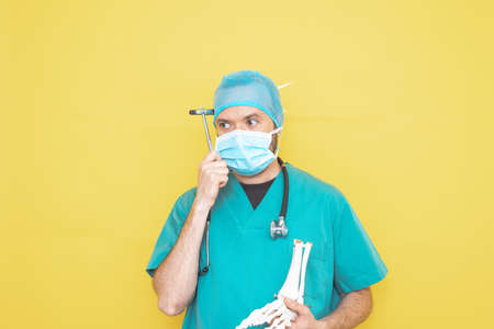 doctor dressed as a surgeon in green with stethoscope and mask on a yellow background with a worried expression.の写真素材