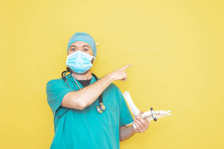 doctor dressed as a surgeon in green with stethoscope and mask on a yellow background with a worried expression.の写真素材