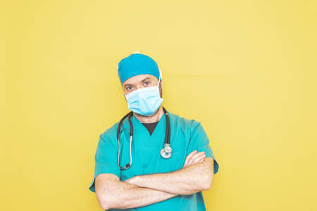 doctor dressed as a surgeon in green with stethoscope and mask on a yellow background with a worried expression.の写真素材