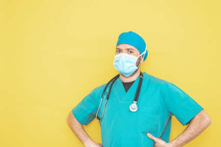 doctor dressed as a surgeon in green with stethoscope and mask on a yellow background with a worried expression.の写真素材