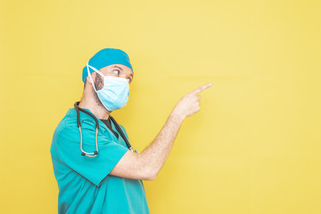 doctor dressed as a surgeon in green with stethoscope and mask on a yellow background with a worried expression.の写真素材