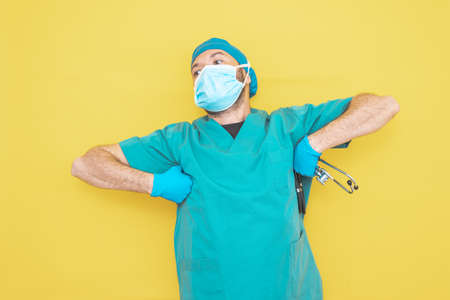 doctor dressed as a surgeon in green with stethoscope and mask on yellow background with gesture pointing to a direction.の写真素材