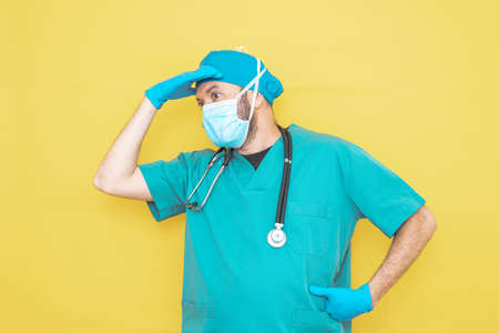 doctor dressed as a surgeon in green with stethoscope and mask on a yellow background with a worried expression.の写真素材