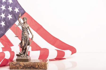 The statue of justice Themis or Iustitia, the blindfolded goddess of justice against a flag of the United States of America, as a legal conceptの写真素材