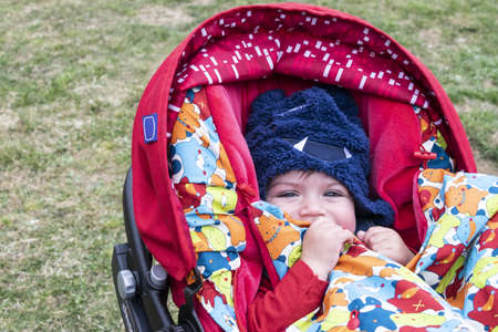 Little boy in pram covered from the cold with hat and blanket. Hello of unseasonably cold weather due to climate changeの写真素材