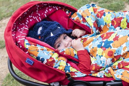 Little boy in pram covered from the cold with hat and blanket. Hello of unseasonably cold weather due to climate changeの写真素材