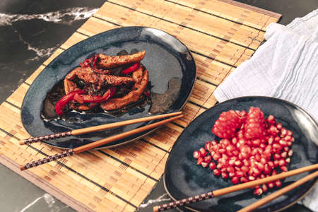Chicken strips with red pepper in teriyaki sauce served with pomegranate seeds for dessert.の写真素材