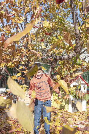 Omage of a 6 year old boys face appearing from underneath autum leaves. The boy is happy with a smile. Leaves have turned brown.の写真素材