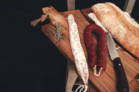 Fuets Catalan dry sausages. Set of spanish sausages and dry cured meat chistorra, chorizo, salchichon, fuet, olives, rosemary, chili peppers on a wooden background. top view.の写真素材