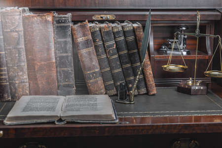 Old quill pen, books and vintage inkwell on wooden desk in the old office against the background of the bookcase and the rays of light. Conceptual background on history, education, literature topics.の写真素材