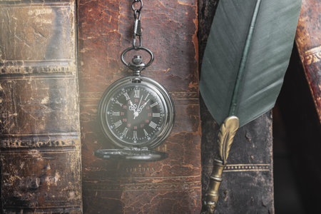 Classic still life with vintage books placed with old clock on rustic wooden background.