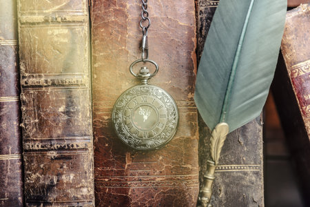 Old quill pen, books and vintage inkwell on wooden desk in the old office against the background of...