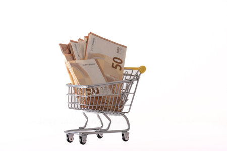 Toy supermarket cart or shopping trolley with money isolated on white background close-up.の写真素材