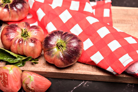 Tiger tomato on a cutting board with basil leaves on wooden background. Fresh tomato wased for cooking. Tomato with droplets of water.の写真素材