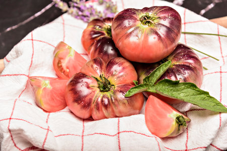 Tiger tomato on a cutting board with basil leaves on wooden background. Fresh tomato wased for cooking. Tomato with droplets of water.の写真素材