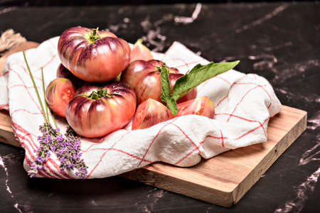 Tiger tomato on a cutting board with basil leaves on wooden background. Fresh tomato wased for cooking. Tomato with droplets of water.の写真素材