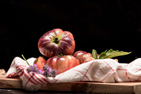 Tiger tomato on a cutting board with basil leaves on wooden background. Fresh tomato wased for cooking. Tomato with droplets of water.の写真素材