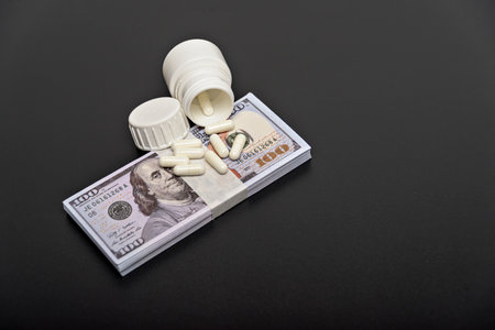 Dollars and white pills on a black background from up close.の写真素材