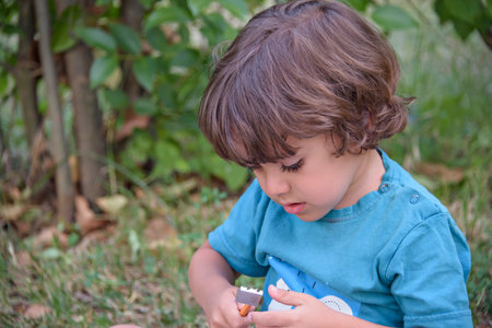 Young Caucasian school boy sitting in park outdoor doing school homework. Child kid writing in notebook with pencil outside. Self education learning studying. Early development for children.の写真素材