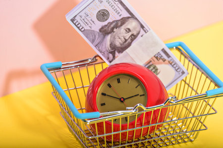 A supermarket trolley with old vintage alarm clock on pink and yellow background. Shopping,...