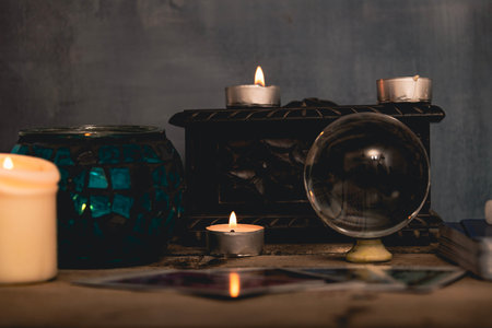 Close-up of a tarot card arrangement with a crystal ball and flickering candles on an aged wooden...