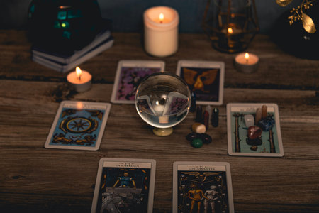 Close-up of a tarot card arrangement with a crystal ball and flickering candles on an aged wooden...